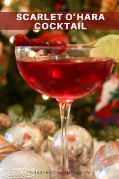 a close up of a wine glass with a drink in front of a christmas tree