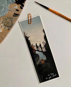 a bookmark with an image of two people on a bridge next to a paintbrush