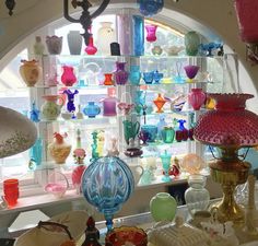 many different colored glass vases are on display in front of a large arched window