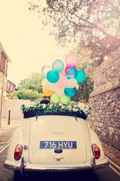 an old car with balloons in the back parked next to a brick wall and cobblestone street