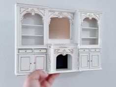 a hand is holding up a doll house built into the side of a white wall