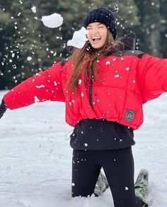 a woman in red jacket throwing snow up into the air with her arms wide open