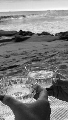 black and white photograph of two people toasting wine glasses on the beach with waves in the background