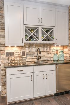 a kitchen with white cabinets and marble counter tops, wine glasses on the cabinet doors