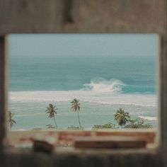 the view from inside an old building looking out at the ocean and palm trees in the foreground