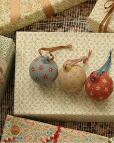 three ornaments sitting on top of a white box next to wrapping paper and twine bows