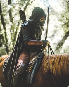 a man dressed in costume riding on the back of a brown horse through a forest