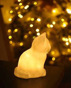 a white cat figurine sitting on top of a table next to a christmas tree