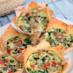 four mini quiches with spinach and cheese on a white plate next to a wicker basket