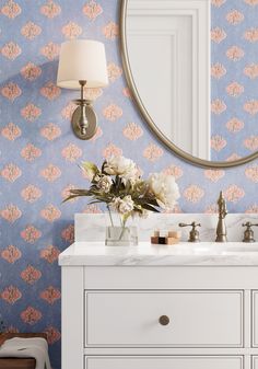 a bathroom vanity with floral wallpaper and a round mirror