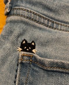 A black cat with white eyes and whiskers embroidered into jeans Embroidery Jean Pocket Ideas, White Cat Embroidery, Jeans Back Pocket Embroidery, Pretty Embroidery Designs, Cute Stitches On Clothes, Black Jeans Embroidery Ideas, Embroidered Jeans Diy Simple, Jean Embroidery Ideas Pockets, Black Jeans Embroidery