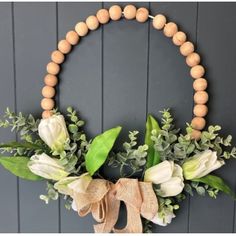 a wooden beaded wreath with white flowers and greenery hangs on a gray wall