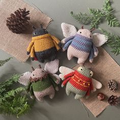 crocheted stuffed animals sitting on top of a table next to pine cones and ferns