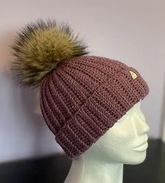 a crocheted hat with a pom - pom on top is shown in front of a mannequin's head