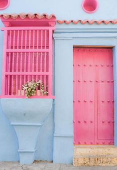 a pink and blue building with two red doors on each side, and a planter in front of the door