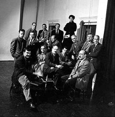 a group of men sitting next to each other in front of a wall with letters on it