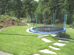 a trampoline set up in the middle of a grassy area with stepping stones