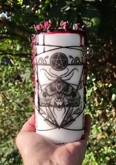 a hand holding up a white candle with black and red designs