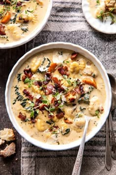 two white bowls filled with soup on top of a gray cloth next to silver spoons