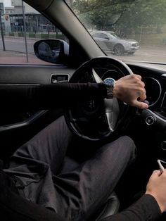 a person driving a car on the street with their hand on the steering wheel while holding a cell phone