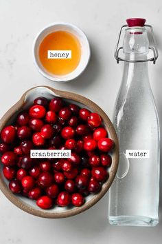 cranberries in a bowl next to a bottle of honey and a cup of water