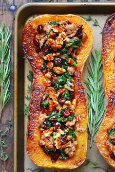 two delicacy squash halves on a baking sheet with fresh herbs and walnuts