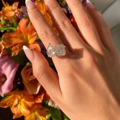 a woman's hand with a ring on her finger and flowers in the background