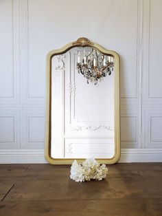 a mirror sitting on top of a wooden floor next to a vase with flowers in it