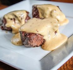 two meatballs covered in gravy on a white plate with a wooden table