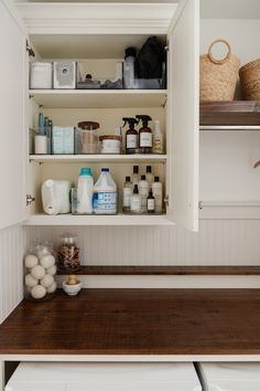 a kitchen with white cabinets and wood counter tops, including an open shelf above the washer and dryer