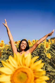 a woman standing in a sunflower field with her arms up and hands raised above her head