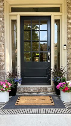 the front door is decorated with flowers and potted plants, along with a welcome mat