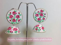 a pair of earrings with flowers painted on the front and back of them, hanging from a metal stand