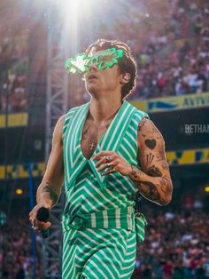 a man in a green and white striped outfit with tattoos on his arm, holding a tennis racquet