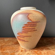 a brown and blue vase sitting on top of a wooden table next to a wall