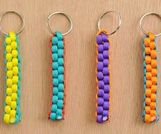 four different colored keychains with metal handles on a wooden surface, one is made out of yarn and the other has an open loop