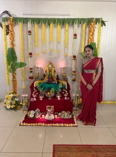 a woman in a red sari standing next to a shrine with flowers and candles