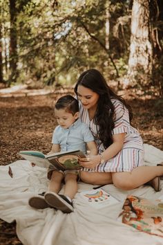 a woman sitting on the ground with a child reading a book in front of her