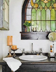 a bathroom sink under a stained glass window in front of a mirror and candle holder