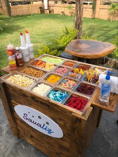 a wooden table topped with lots of trays filled with different types of food next to a tree