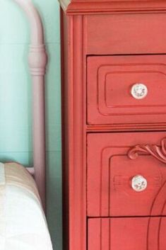 a red dresser next to a bed in a room with blue walls and pink furniture