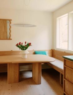 a vase with flowers sitting on top of a wooden table next to a bench in a room