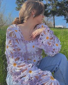 a woman sitting in the grass wearing a purple crochet top with flowers on it