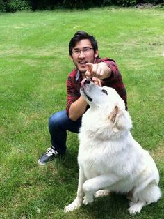 a man kneeling down next to a white dog on top of a grass covered field