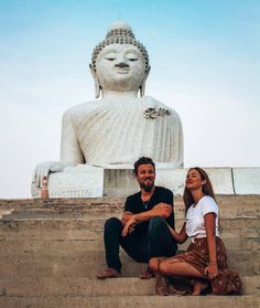 a man and woman sitting on steps in front of a large buddha statue with their arms around each other