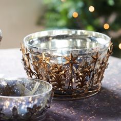 two metal bowls sitting on top of a table next to a christmas tree with lights in the background