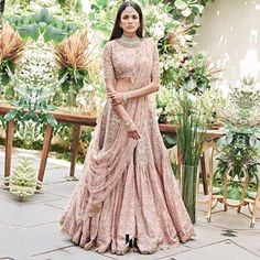 a woman in a pink lehenga standing on a patio with greenery behind her