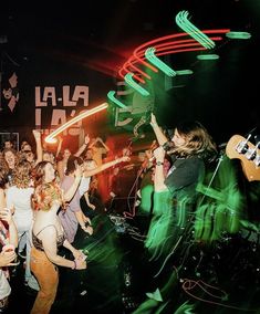 a group of people standing around each other at a music concert with their arms in the air