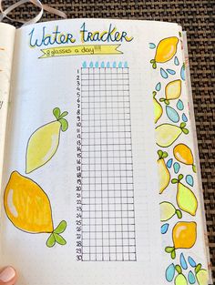 a hand holding an open notebook with water tracker on the page and lemons drawn on it