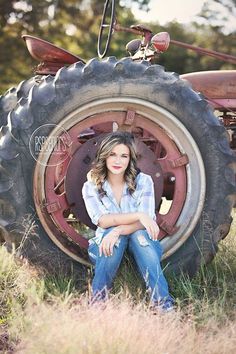 a woman is sitting in front of an old farm tractor with her hands on her knees